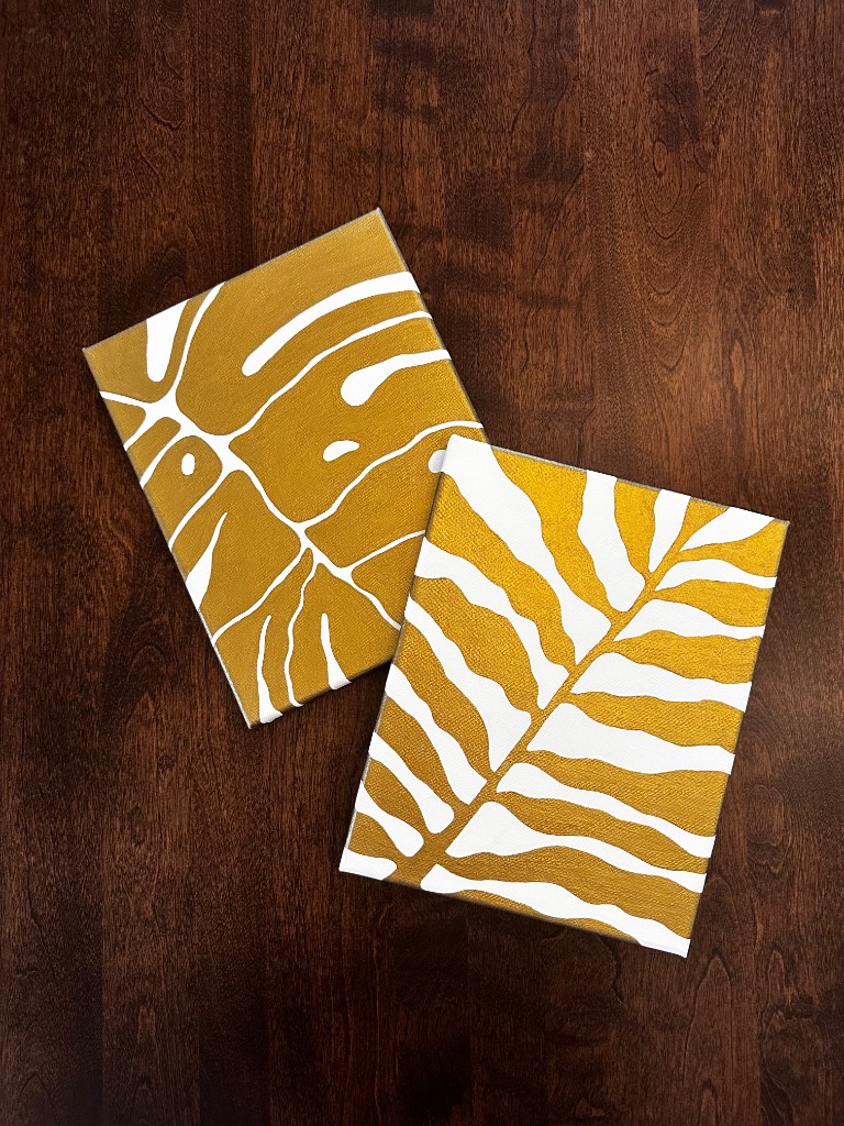 Two gold botanical canvases resting on dark wood